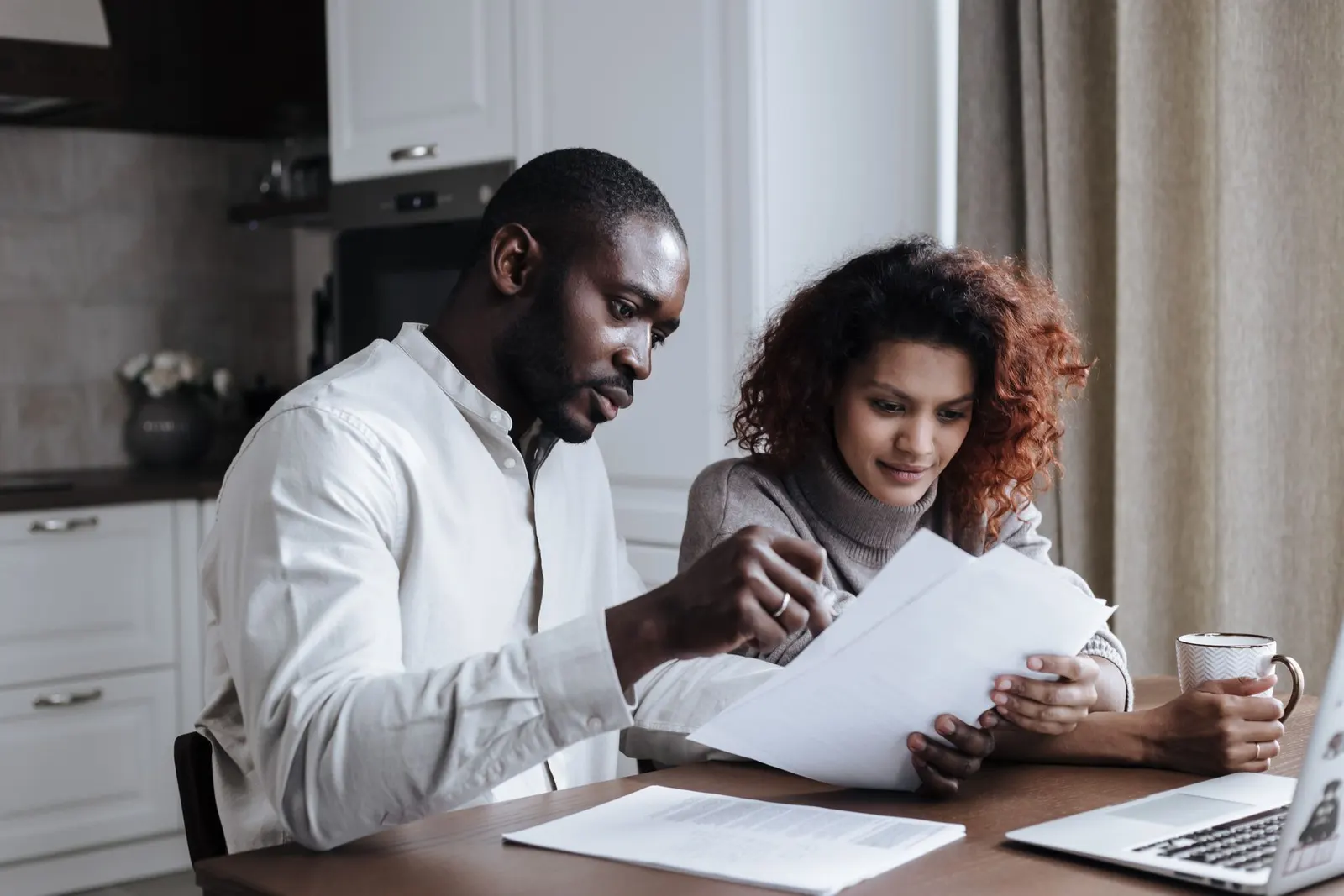 A couple working through documents together on a laptop at home.