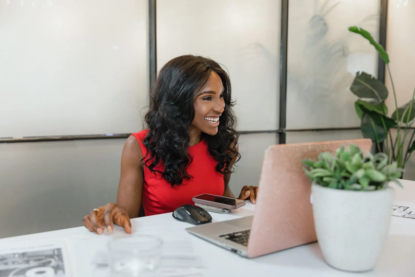 A professional woman smiling at her desk with a laptop and smartphone.