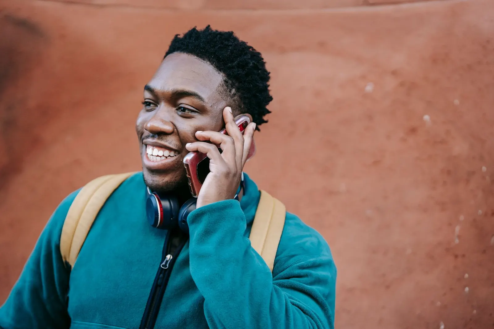 A cheerful young man with a backpack talking on his phone in the street.