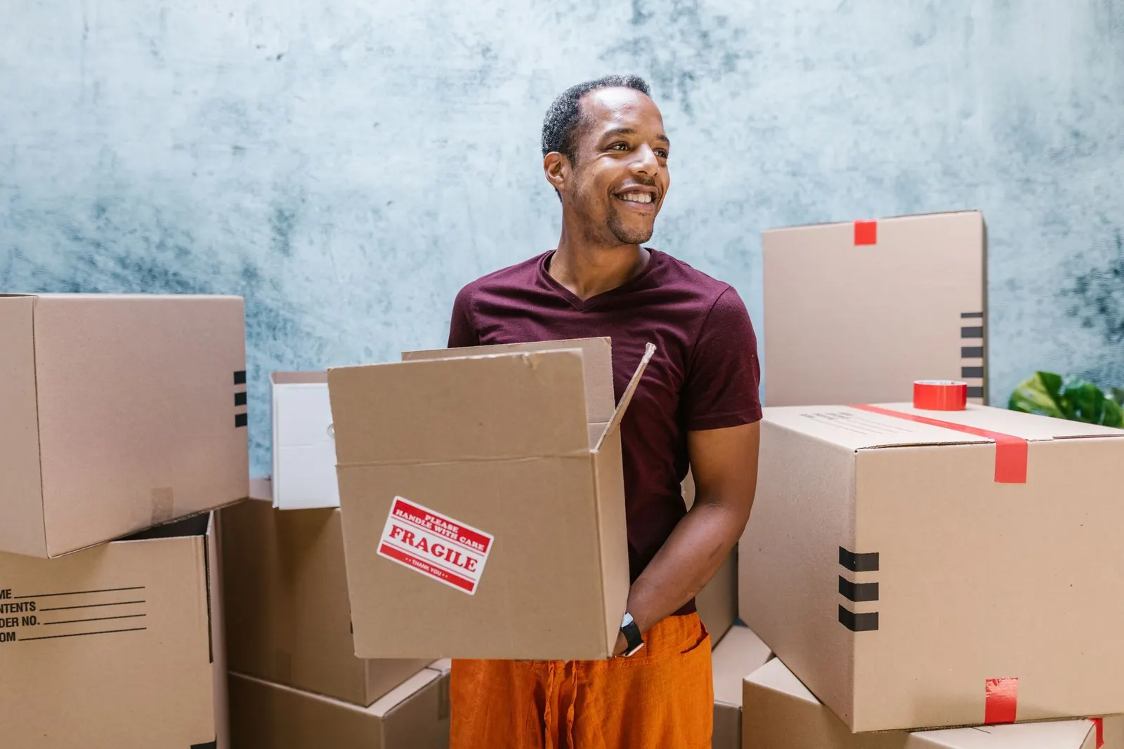 A smiling business owner holding a box among stacked parcels ready for delivery.