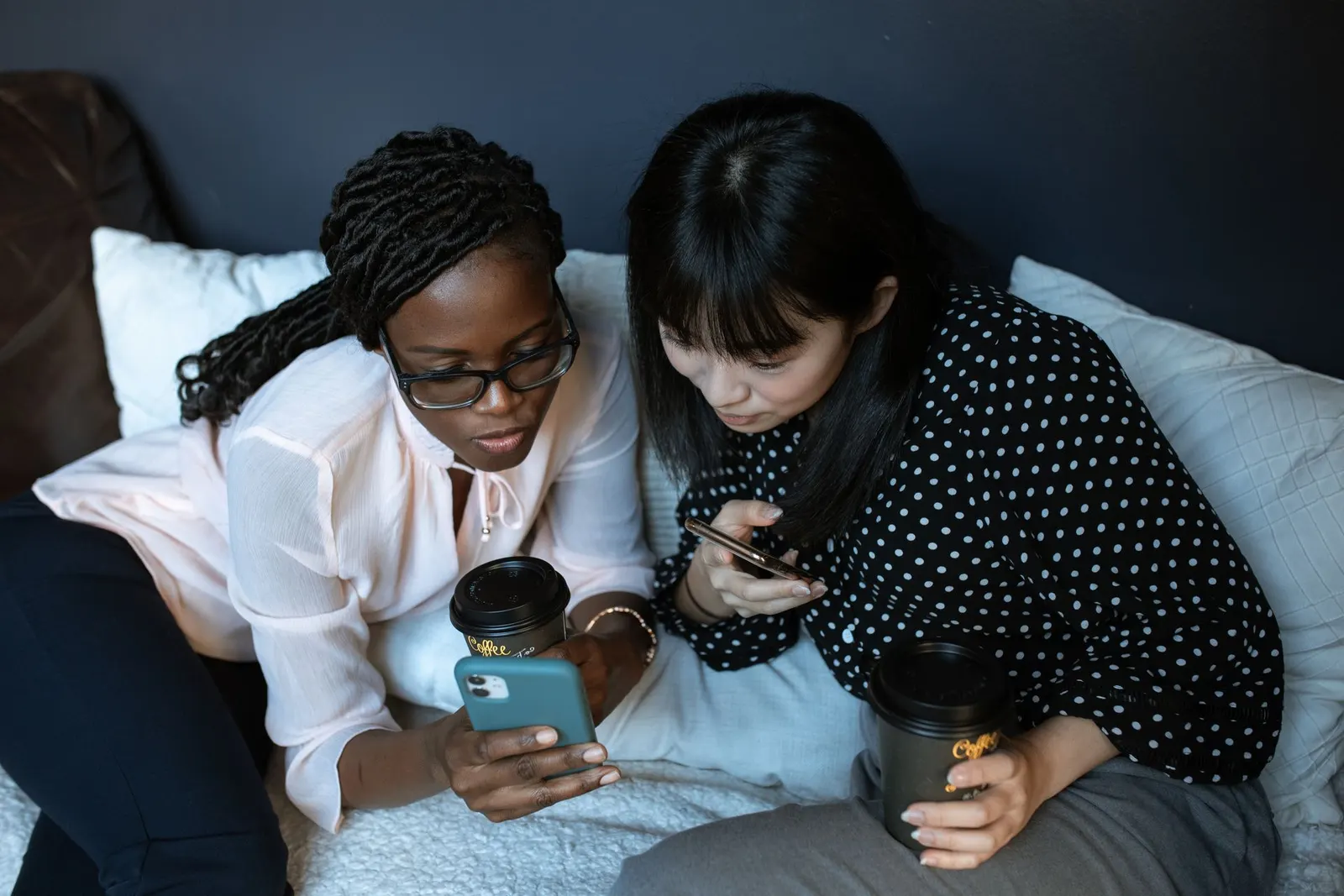 Two women sitting together, one showing the other something on her phone.